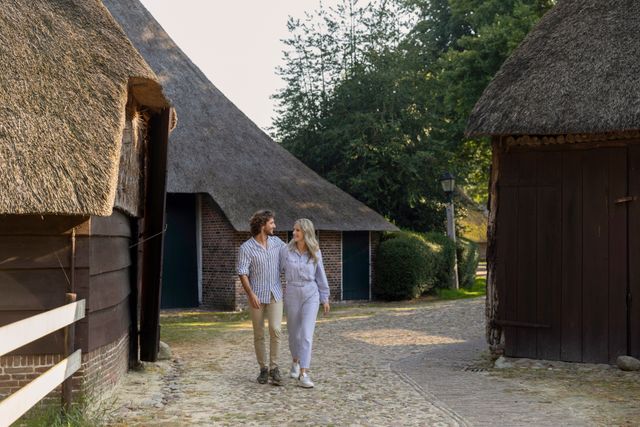 Man en vrouw wandelen door monumentendorp Orvelte, langs mooie rietgedekte boerderijen.