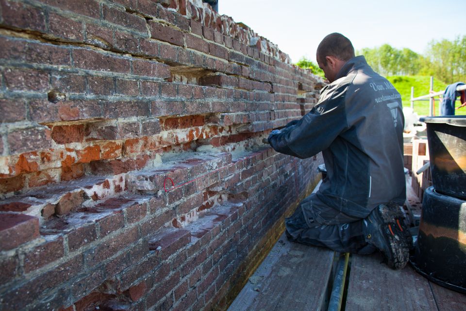 Man is voegen en bakstenen aan het restaureren op Fort de Waalse Wetering