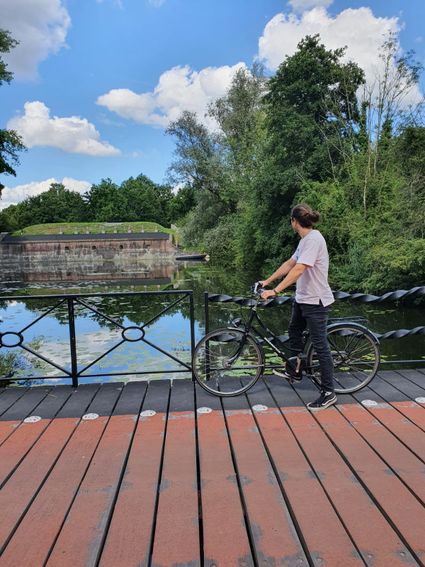 Een man staat met zijn fiets op een brug te kijken naar een fort in het water.