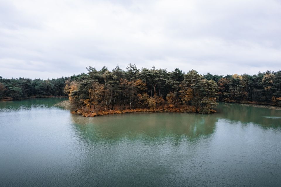 Een blauw meer met bos in herfstkleuren.