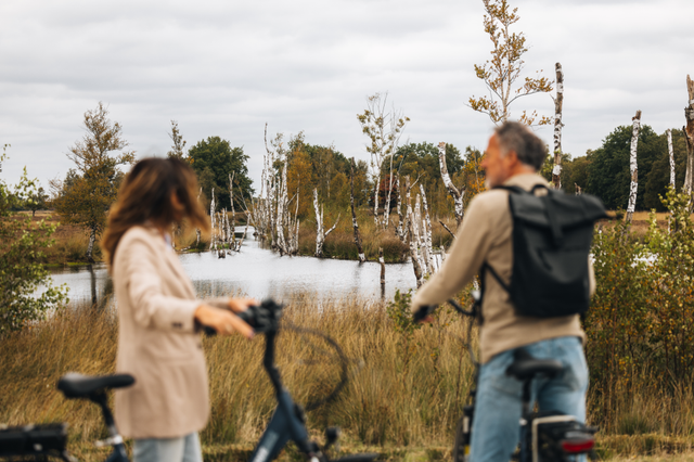 Een man en een vrouw zijn in het Bargerveen even van de fiets afgestapt om van het veenlandschap te genieten.