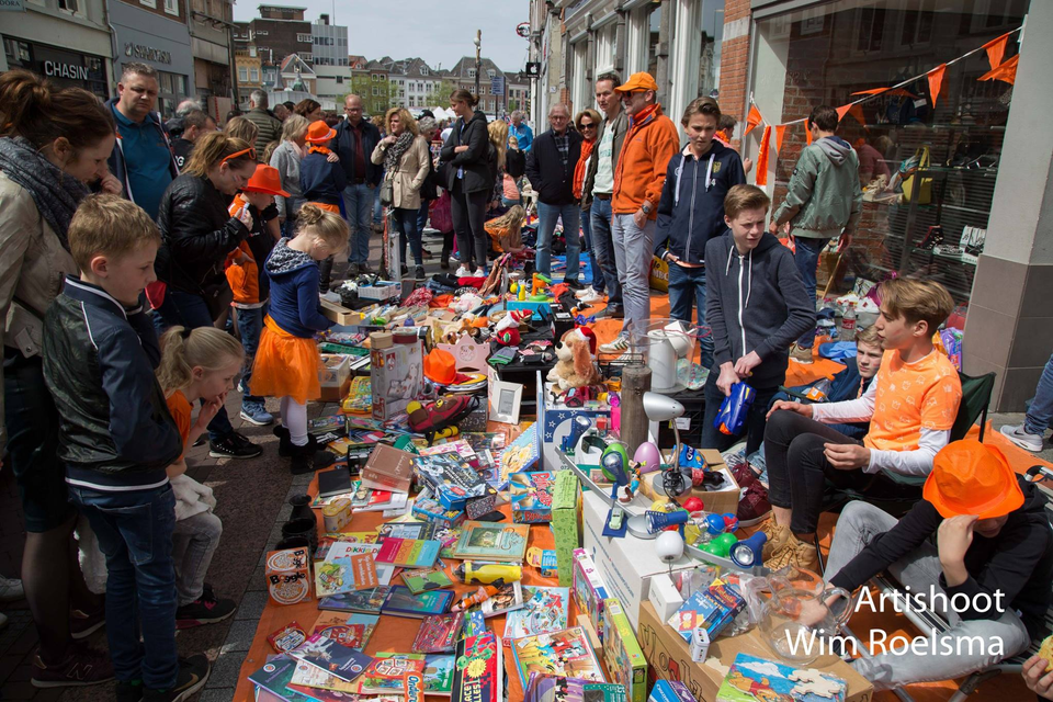Foto van een rommelmarkt op Koningsdag waar veel mensen op te zien zijn met allerlei te verkopen spullen