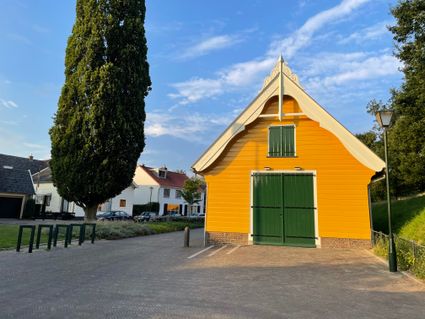 Een geel, houten gebouw, met een groene deur.