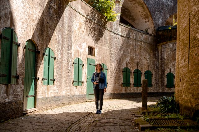 Een jonge vrouw met een fotocamera wandelt lachend door een rondgang in een bakstenen fort.
