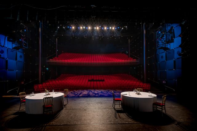 Theaterzaal met twee tafels op het podium en stoelen op het podium en een lege theaterzaal.