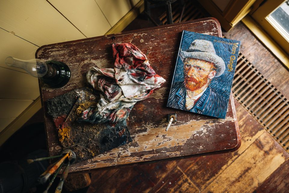 Een tafel met kwasten, doeken, een petroleumlamp en een boek over Van Gogh in de kamer waar hij gewoond en gewerkt heeft in Drenthe,