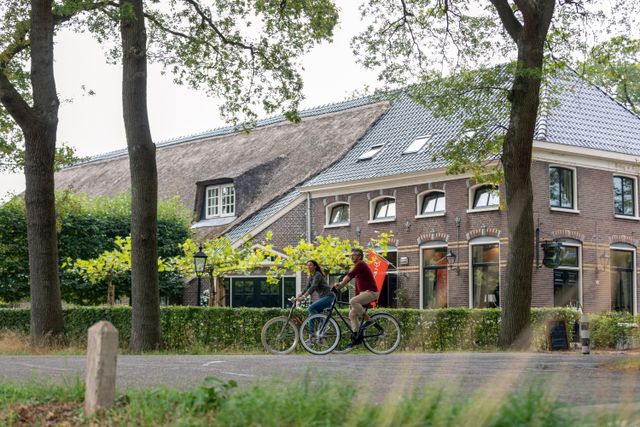Een man en vrouw fietsen in een Drents dorp voor een oude boerderij langs.