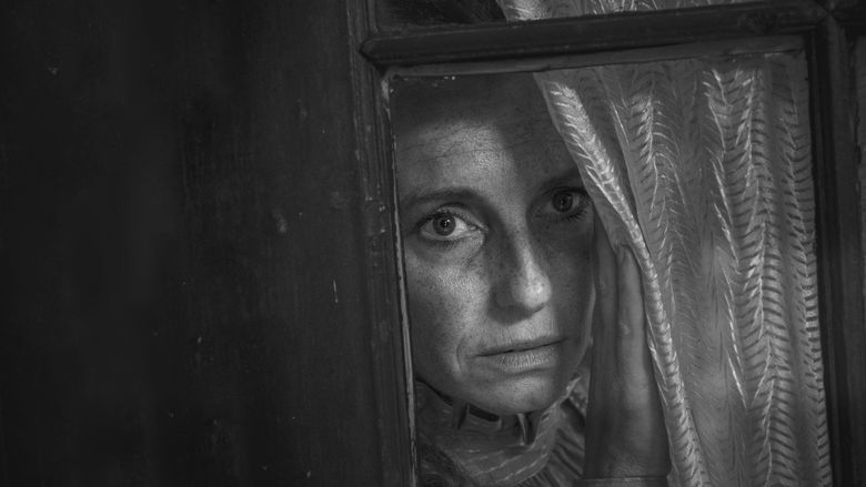 Zwart-wit foto van een vrouw met een angstige blik in de ogen die door een raam kijkt