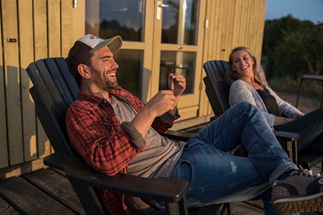 Een man en een vrouw zitten lachend op hun stoel voor een vakantiehuisje.