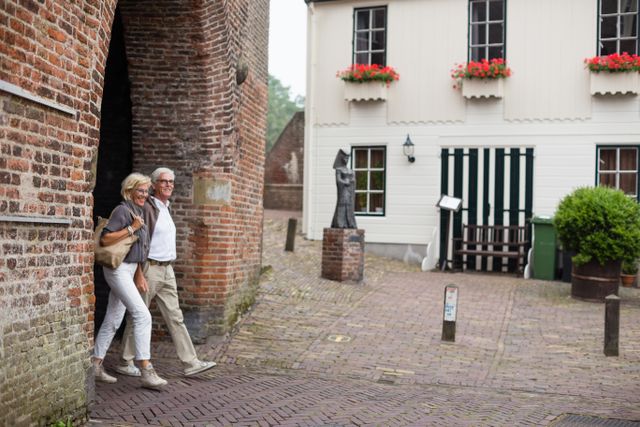 Een oudere man en vrouw lopen samen onder een bakstenen poortje door in een stadje.