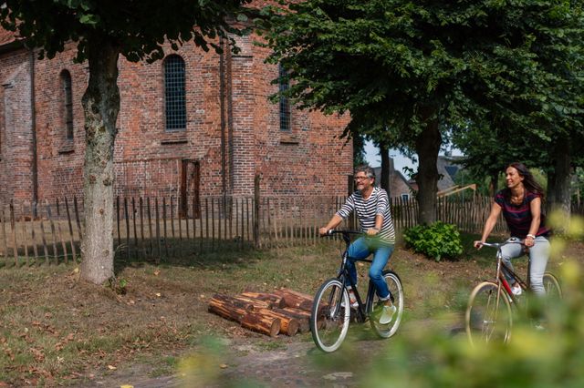 Een man en vrouw fietsen langs een kerk door een dorp.