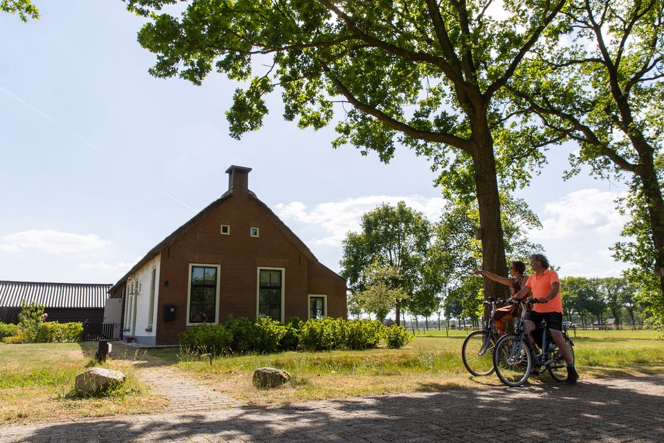 Twee fietsende mensen die kijken en wijzen naar een koloniehuisje in Frederiksoord