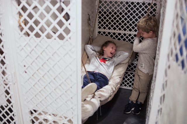 Een meisje is op het bedje in een vroegere cel gaan liggen en daar moeten zij en een jongetje erg om lachen.