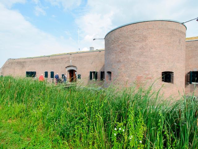 een groep bezoekers betreedt een bakstenen fort, omgeven door planten.