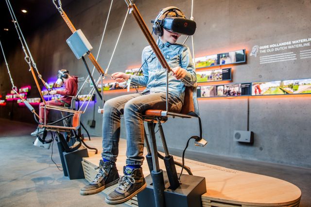 Twee kinderen zitten in een speciale experience met een schommel en een VR-bril in het Waterliniemuseum.