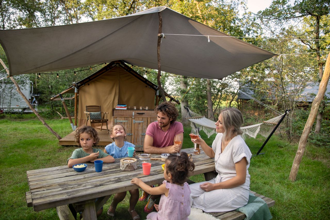 Een gezin op de camping zit aan een picknicktafel.