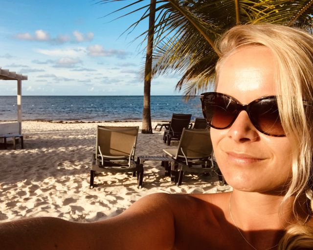 Een selfie van een vrouw met een zonnebril op het strand waar de zon schijnt.