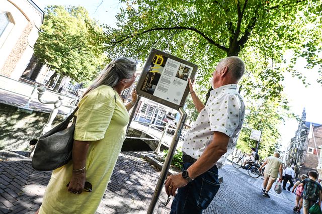 Schuin beeld van een ouder stel die informatie leest op een Vermeerkubus in de zomer in Delft
