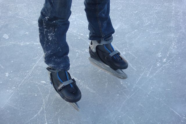 Foto van iemand die op natuurijs aan het schaatsen is. Je ziet alleen de benen en schaatsen van de persoon.