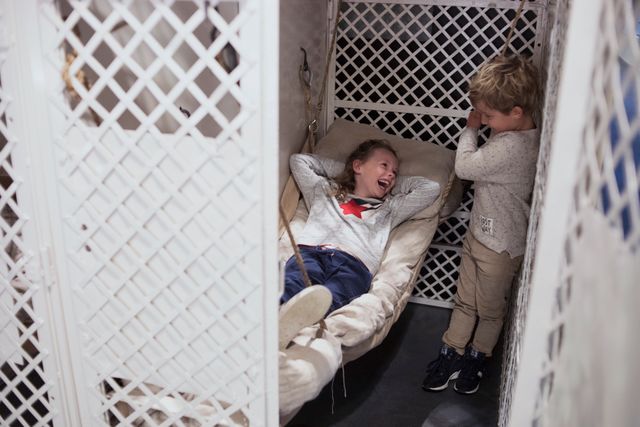 Een jongen en meisje zijn in het Gevangenismuseum. Het meisje is op het bedje in een vroegere cel gaan liggen en daar moeten ze alletwee erg om lachten.