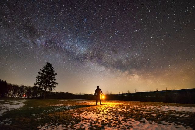 Man loop in het donker in de natuur met een sterrenhemel op de achtergrond.