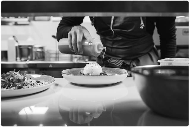 Een zwart wit foto van een kok in TWAALF Restaurant en Bar die een gerecht afmaakt