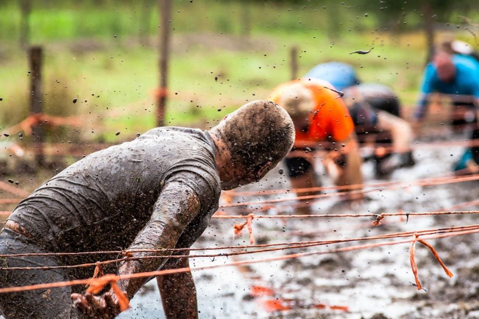 Mensen kruipen door de modder tijdens een mud run.
