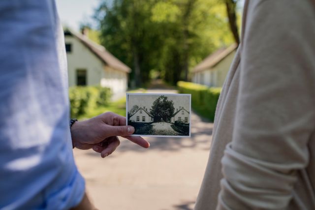 Op de voorgrond wordt een oude foto vastgehouden van koloniehuisjes in Frederiksoord die je op de achtergrond ziet.