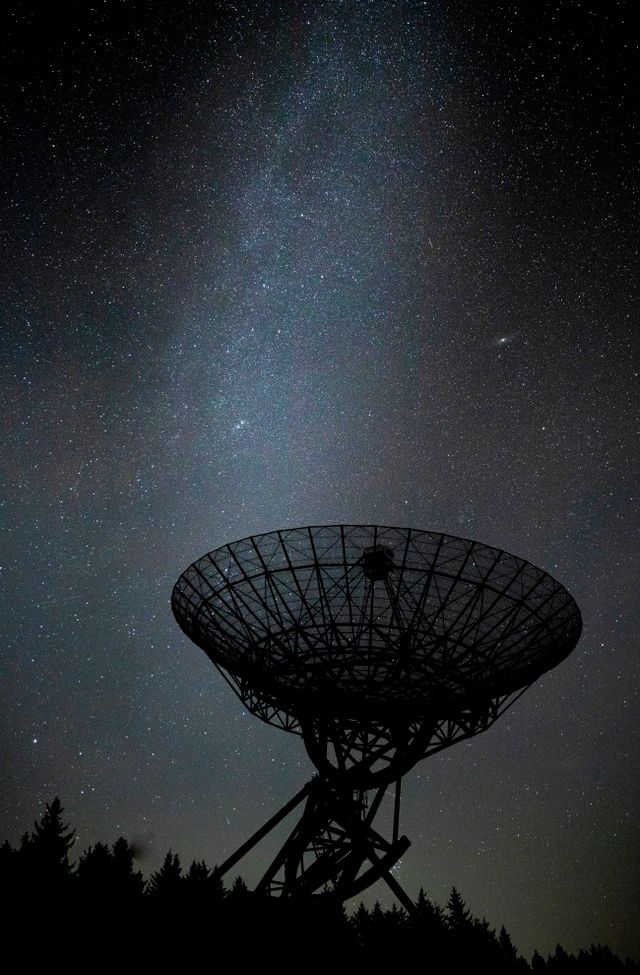 1 van de 14 antennes van de Sterrenwacht bij Westerbork in de nacht. het is ontzettend donker, waardoor je de sterren en de melkweg heel goed ziet. Er schitteren duizenden sterren aan de hemel.