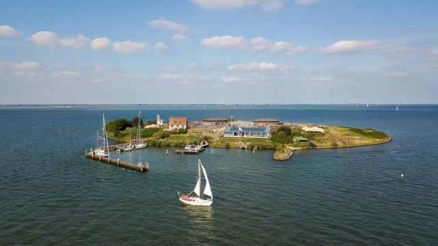 Het forteiland Pampus vanuit de lucht gefotografeerd. In de voorgrond van de foto zeilt een witte zeilboot.
