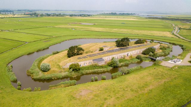 Fort bij Krommeniedijk vanuit de lucht gefotografeerd. Er omheen zie je weilanden, een klein buurtschap en een waterpartij.