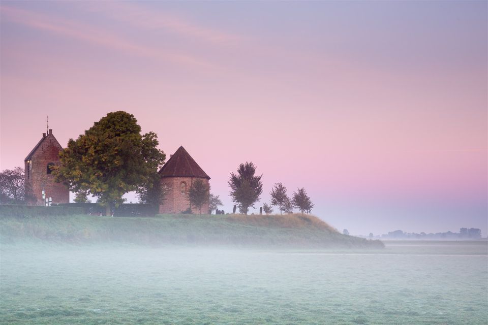 Foto van een Gronings landschap met weiland, een kerkje en mist bij de opgaande zon