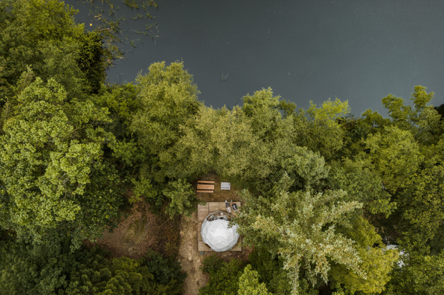 Een droneshot van de overnachtingsdome op het bosrijke natuurkampeerterrein Mariahoeve aan de rand van het pingomeer.