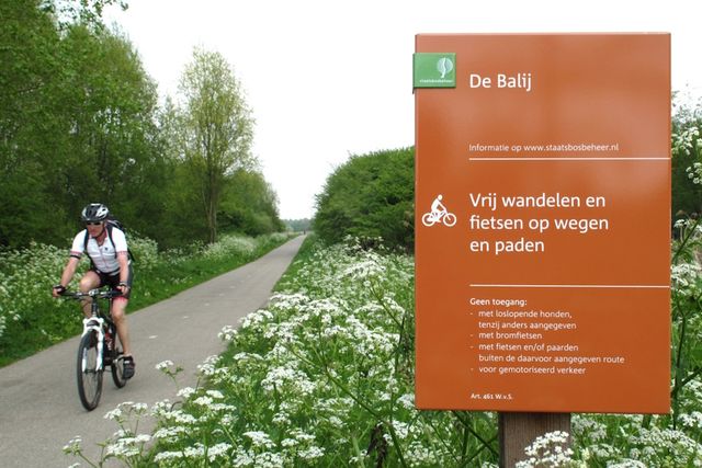 Een mountainbiker rijd over een pad met een bord aan de zijkant van de weg staat een bord.