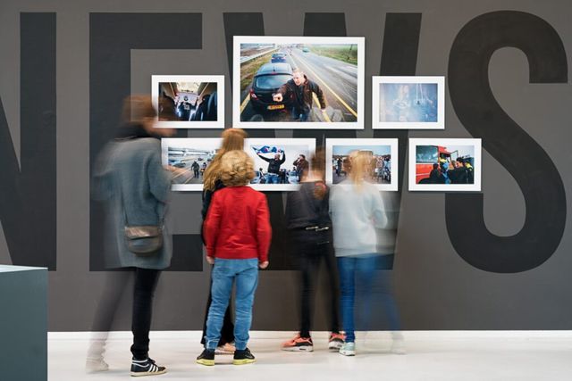 Een vrouw en vier kinderen kijken naar foto's aan de wand in een tentoonstelling in Museum Hilversum.