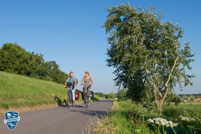 Echtpaar fietst over asfaltweg in een groene omgeving in of rondom Flevoland.