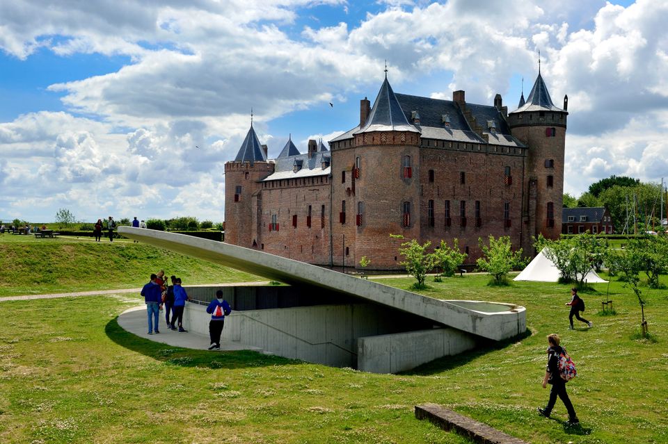 Kasteel Muiderslot van een afstandje gezien. Op de voorgrond bewonderen bezoekers het kasteel.