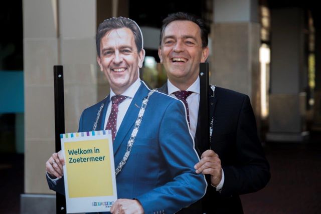Een foto van de burgemeester van Zoetermeer, Michel Bezuijen. Hij heeft een bordje vast met de tekst Welkom in Zoetermeer.