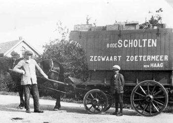 Een oude zwart-wit foto van twee mannen die voor een paard staan met een trekwagen er achter.