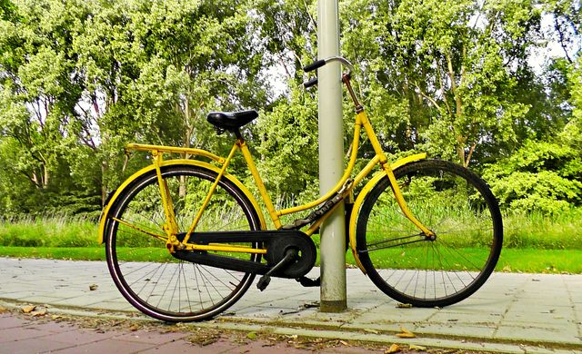 Een gele fiets staat tegen een lantaarnpaal aan. Hij is vastgemaakt met een slot.