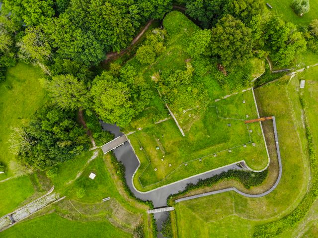 Een luchtfoto van een bakstenen fort overgroeid met gras. Aan de ene helft van het fort zijn de planten op het fort laten staan, de andere helft van het fort is kaal gemaakt.