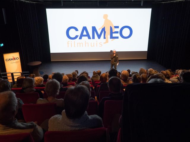 Een filmzaal met mensen en een groot doek waar Cameo op staat.