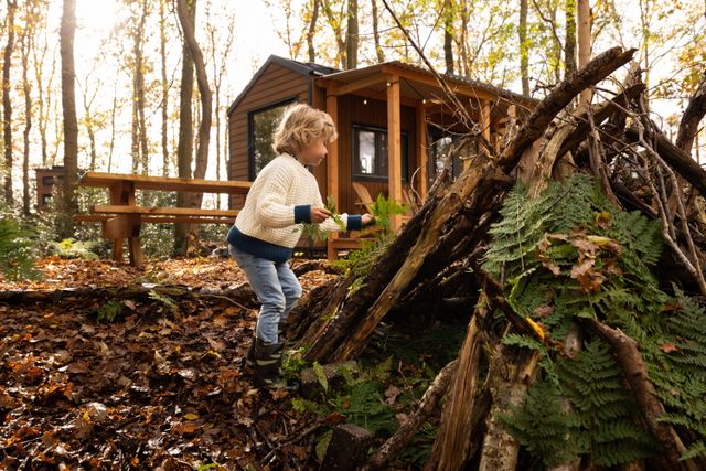 Een jongetje speelt met bladeren voor een Tiny House in het bos.