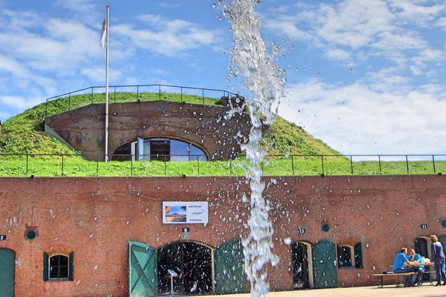 Een bakstenen fort van voren gefotografeerd. Op de voorgrond spuwt een fontein water.