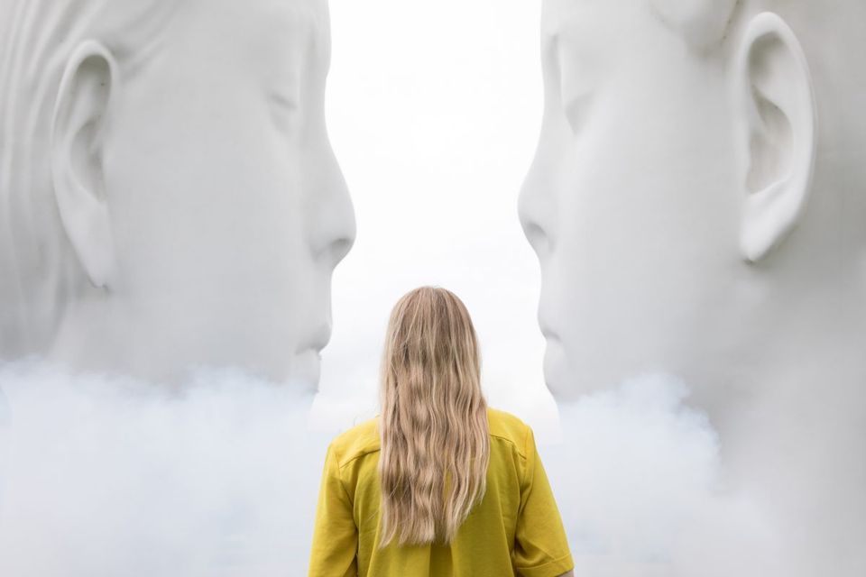 Vrouw staat in de mist tussen de twee grote gezichten die samen de 'LOVE' fontein vormen