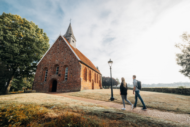 Een man en een vrouw lopen over het pad naar de ingang van het kerkje van Zweeloo.