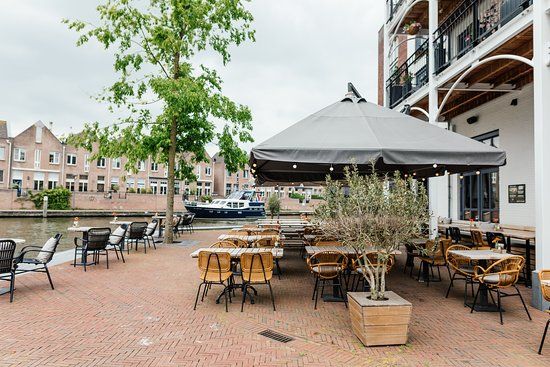 Een leeg terras met rechts daarvan het restaurant en op de achtergrond de Oude Rijn en huizen.