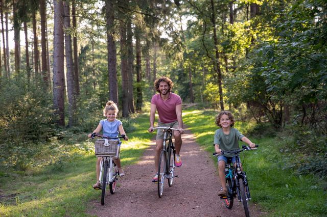 Een vader fietst in de zomer lachend door het bos met zijn twee kinderen.