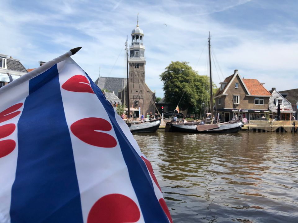 Een in focus friese vlag op de achterkant van een boot. Je ziet zomers lemmer wazig in de achtergrond.