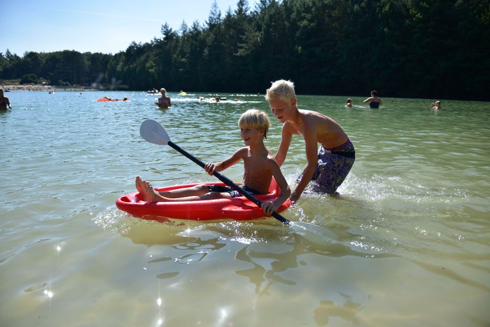 Kinderen zwemmen in de zwemplas, met een jongen in kano op de voorgrond.
